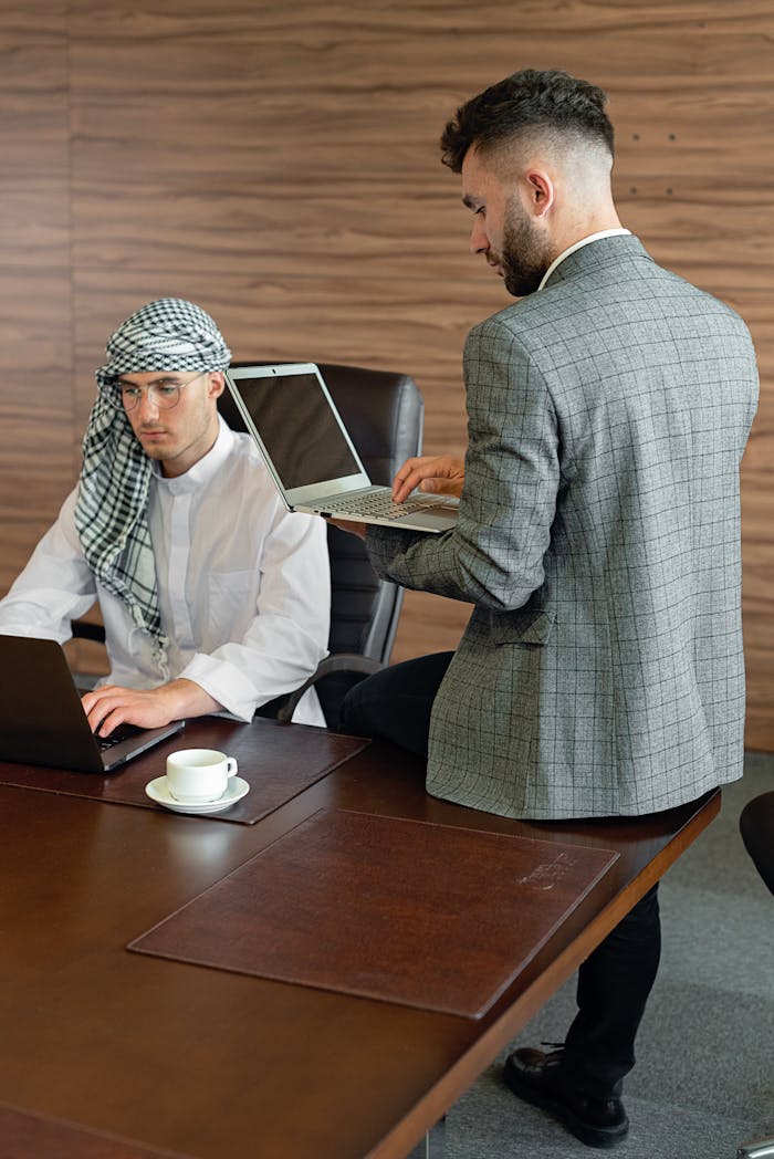 Two male professionals collaborating on laptops in a modern office setting.